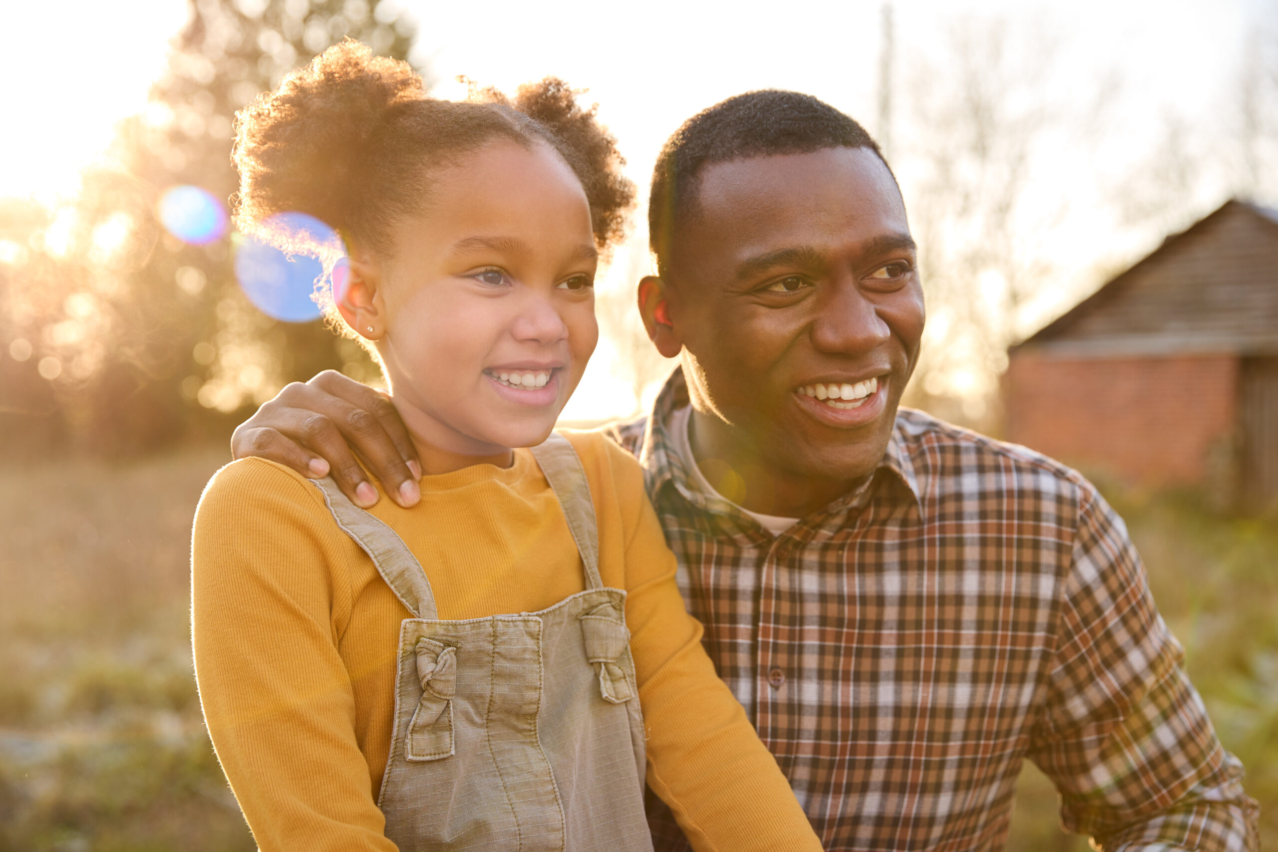 Portrait Of Smiling Father And Daughter Outdoors In Autumn Countryside Against Flaring Sun