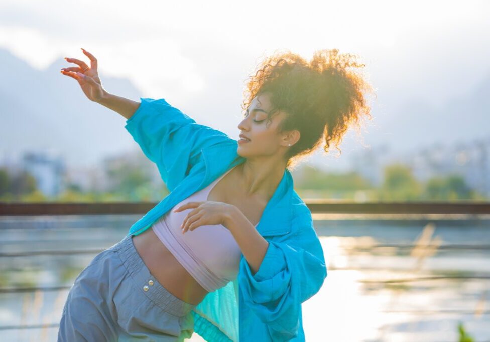 mixed race curly woman enjoying dance at sunset in beach .