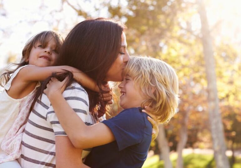 mother-carrying-son-and-daughter-as-they-play-in-park-picture-id660353478