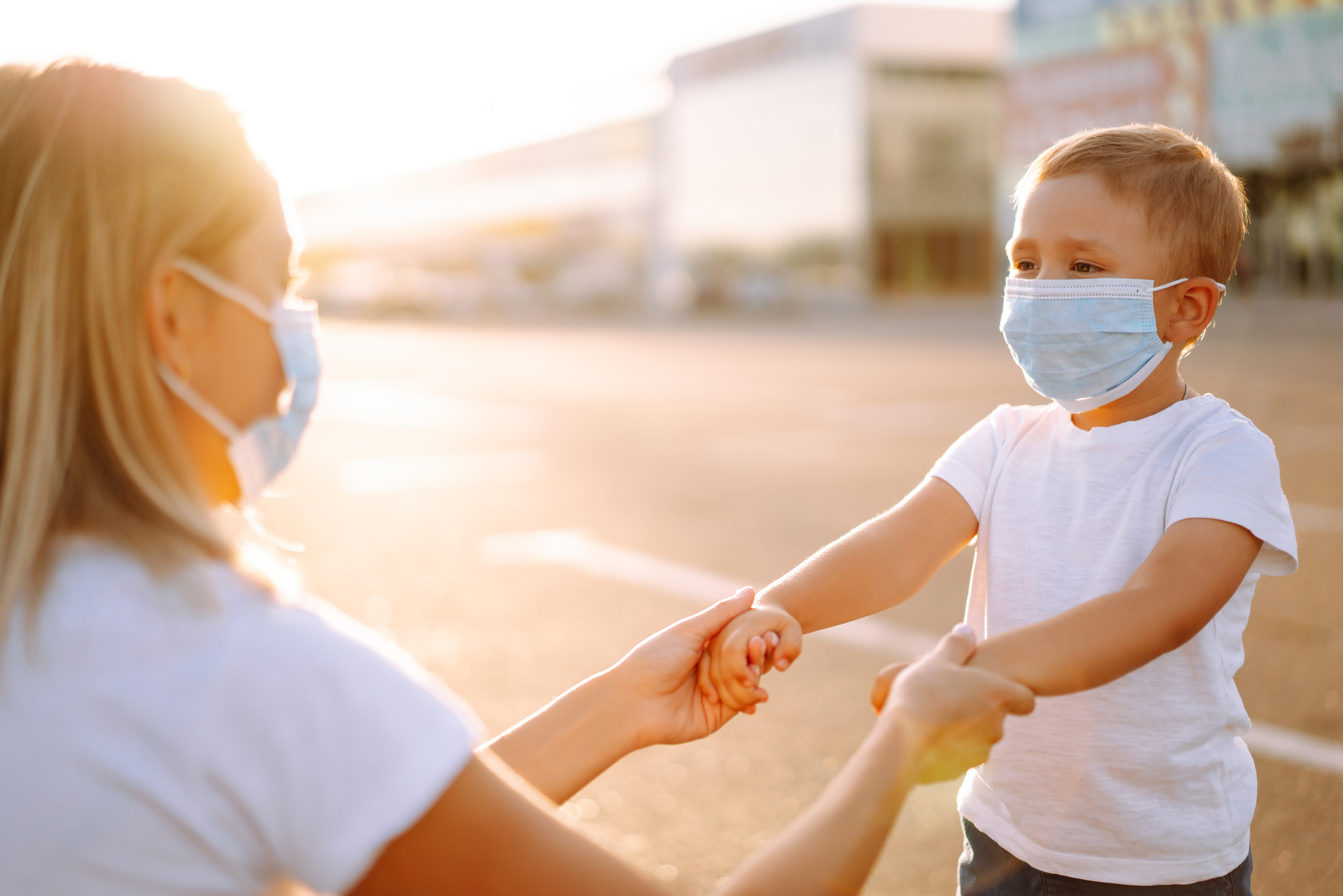 Mother puts on her baby sterile medical mask at sunset during pandemic. Little boy and mom in medical mask.